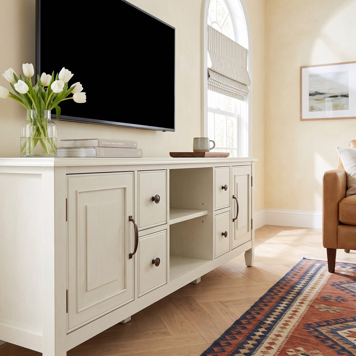 Closer view of the white tv stand doors, drawers and open bay in the same sunlit den with a patterned rug