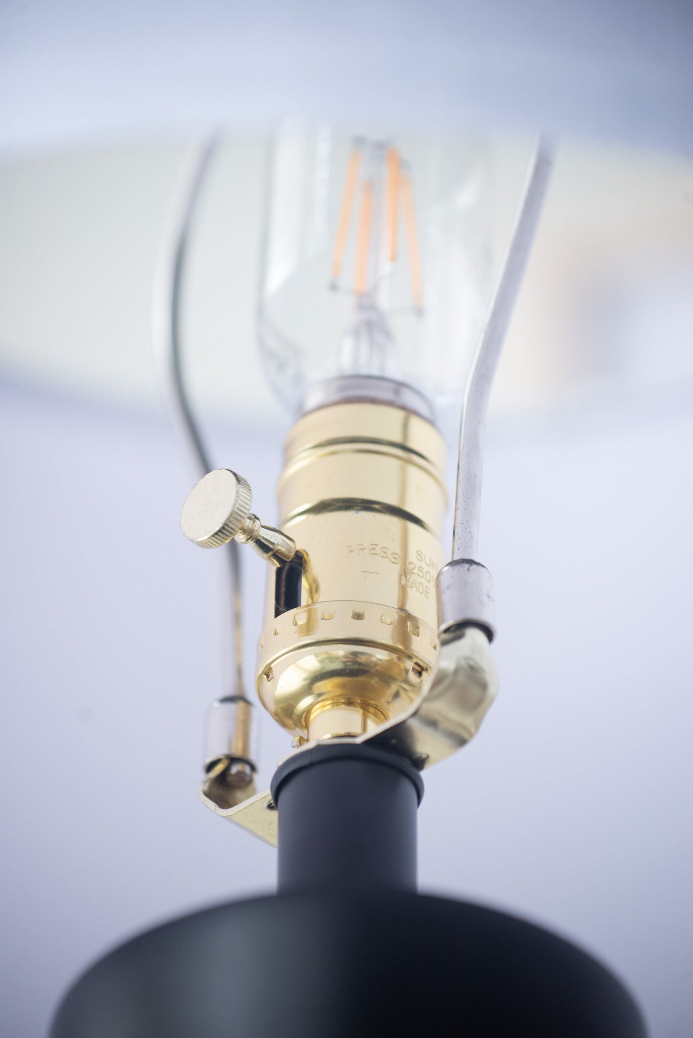 Close-up of a black and gold lamp with a clear glass shade against a light gray background