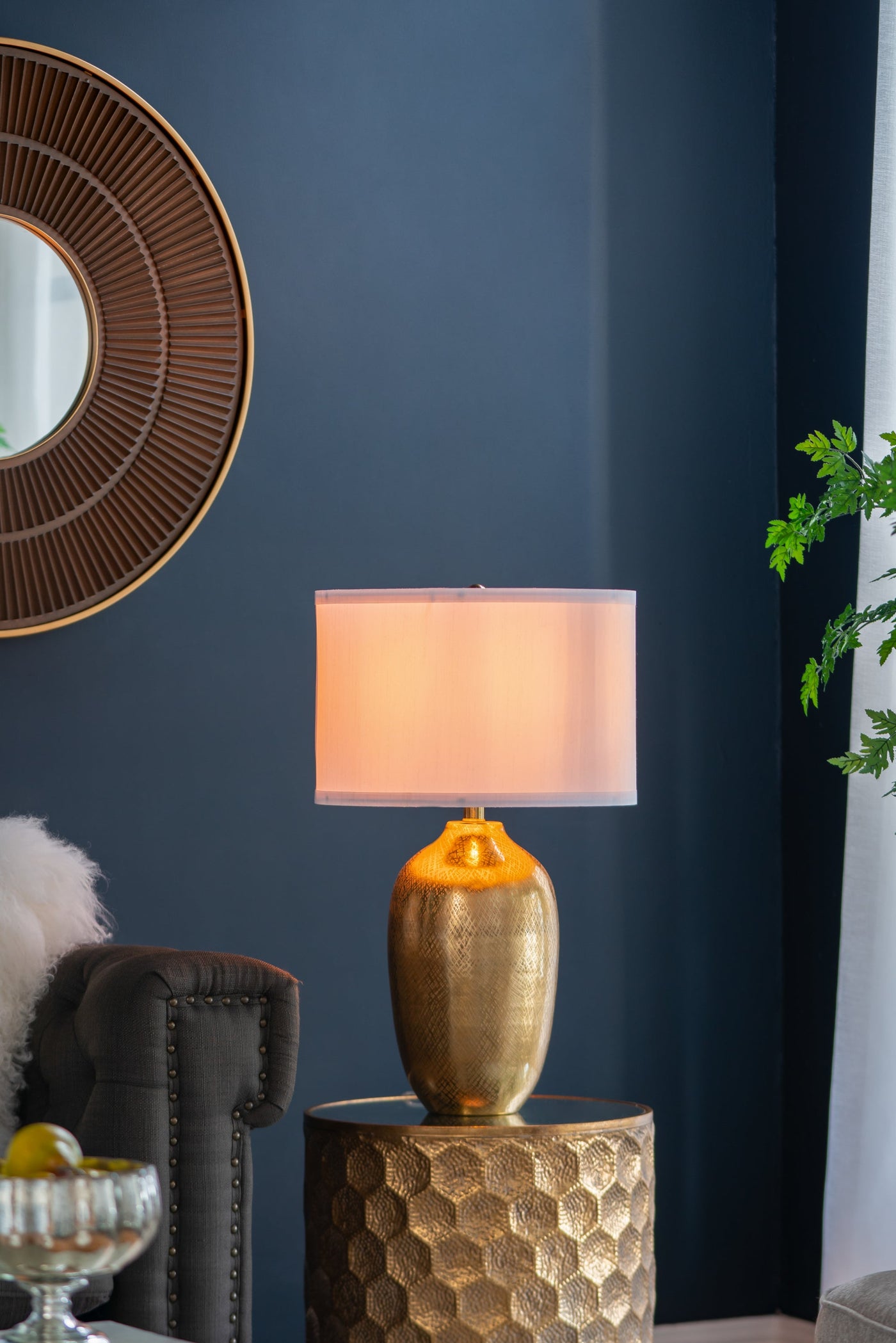 Gold table lamp on a textured side table against a dark blue wall.
