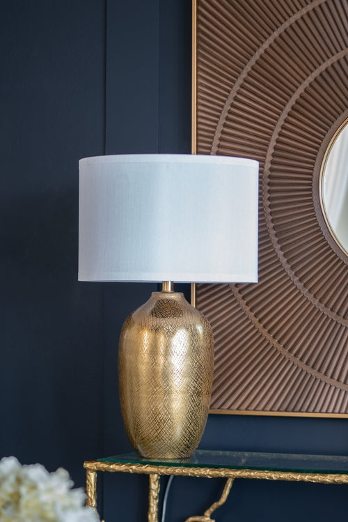 Gold textured table lamp with a white shade on a dark blue wall background