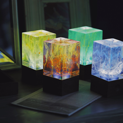 Four colorful cube-shaped lamps on a dark surface with a blurred background