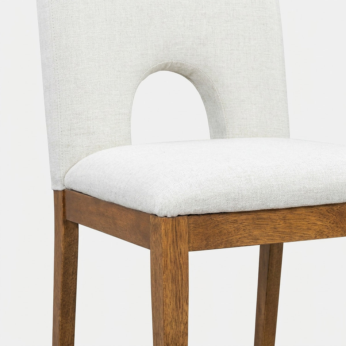 Close-up of a half-round hollow chair back and cream linen seat with a walnut leg