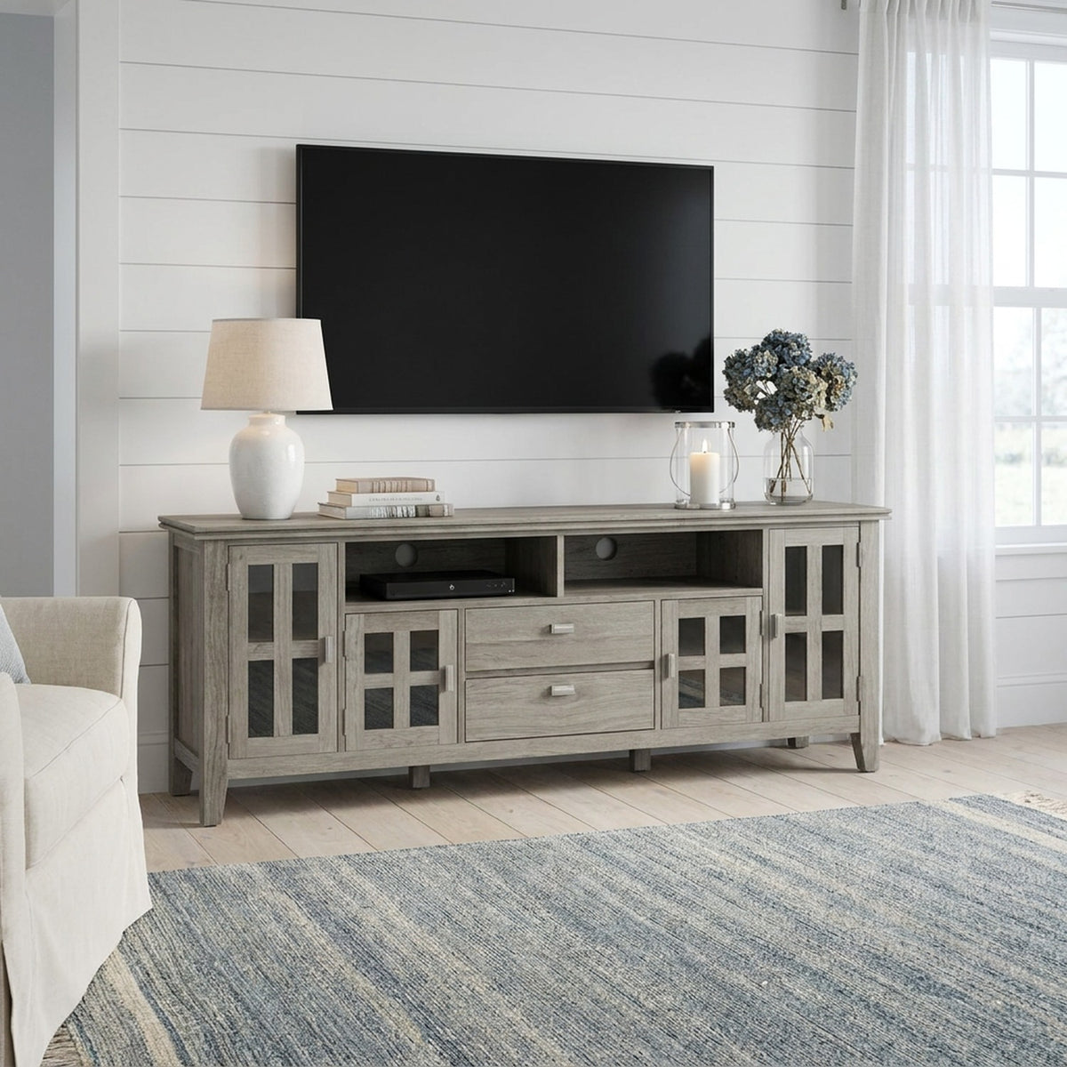 TV stand beneath a wall-mounted TV in a bright coastal living room with white shiplap walls