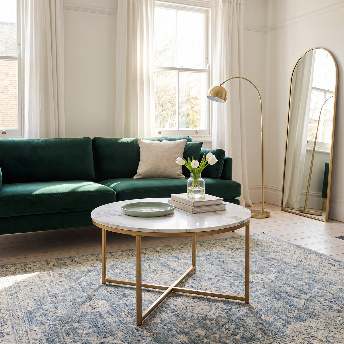 Round white faux-marble coffee table with gold base beside a green sofa, seen from the side in a living room