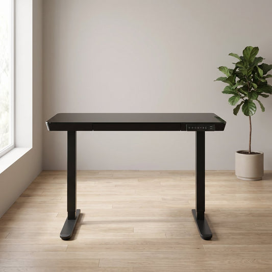 Black glass-top electric standing desk on twin steel legs beside a window and a fiddle-leaf fig in a home office