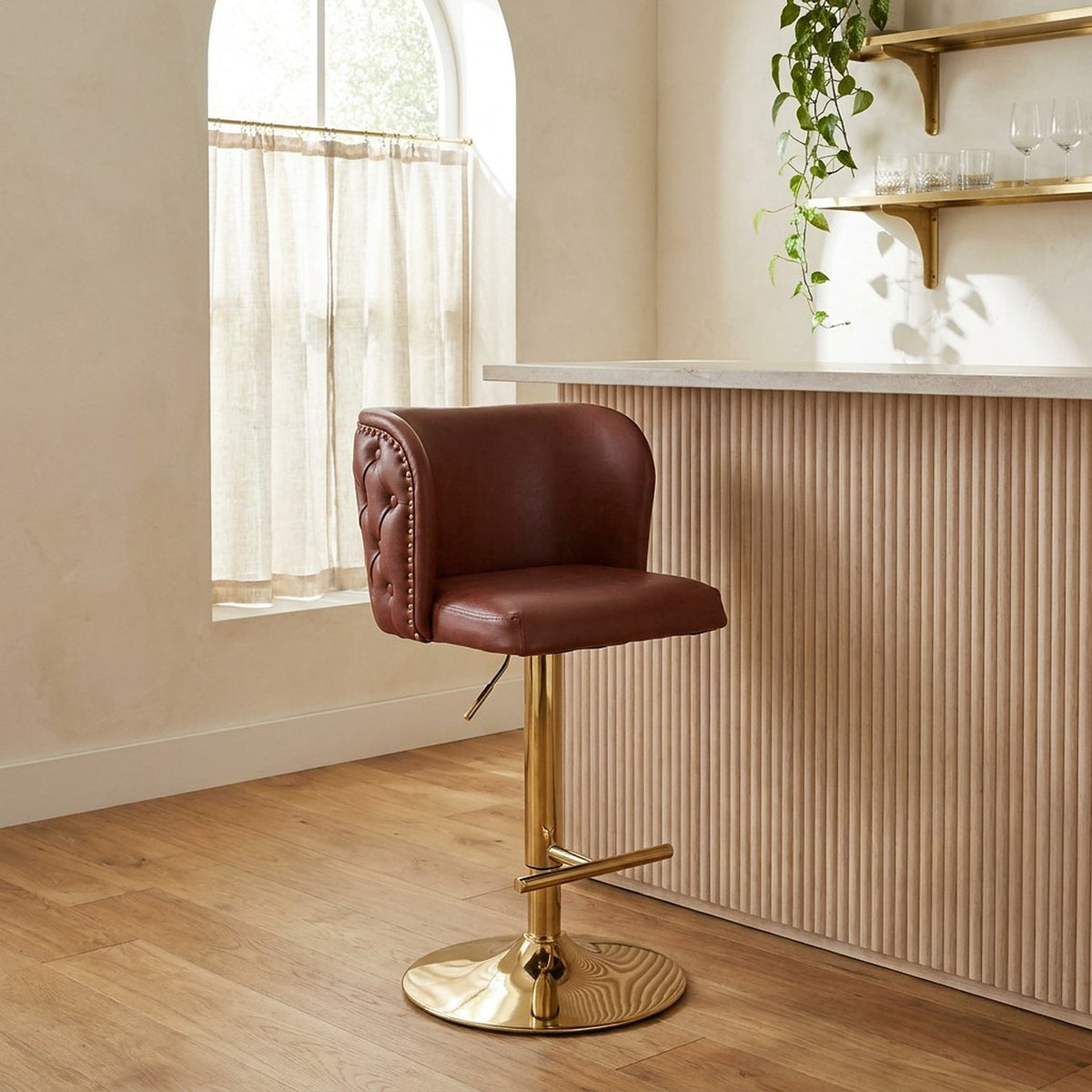 Burgundy leather swivel stool with a gold base at a fluted oak breakfast bar in morning light
