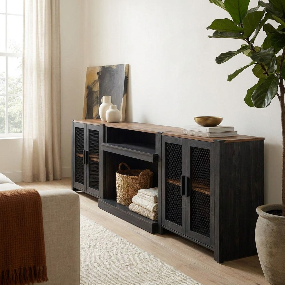 Right-side angle of the black 100 inch tv stand with a basket and folded throws on the open shelf in a living room