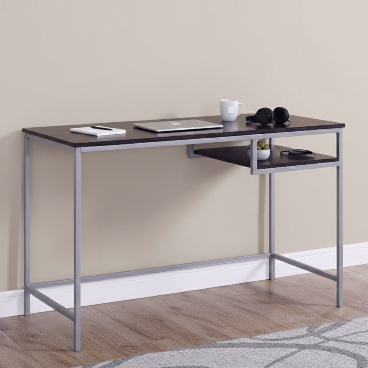 Modern desk with a dark surface and metal frame against a beige wall.