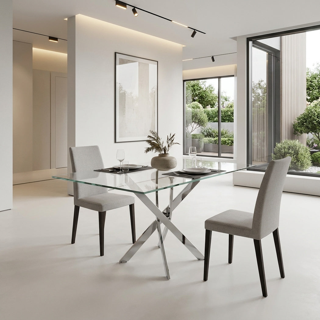 Glass dining table with chrome legs set for four in a bright dining room beside full-height garden windows