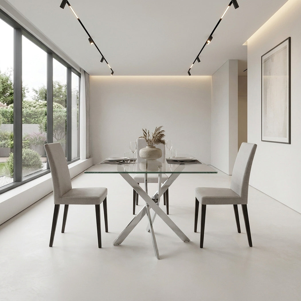 Glass dining table with chrome legs seen down the length of a bright dining room, window wall to one side