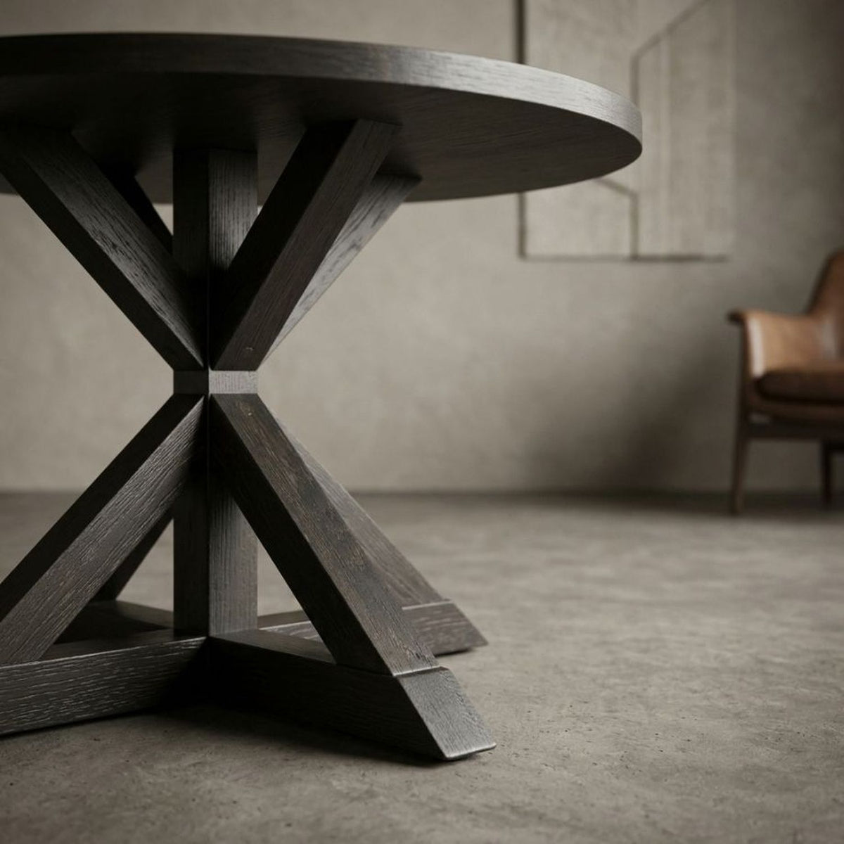 Black round table on a cross-buck base in a grey concrete loft beside a leather lounge chair