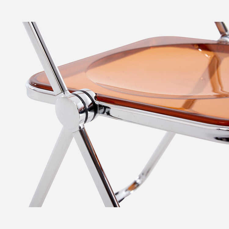 Close-up of a chair with a transparent yellow seat and metallic frame on a white background