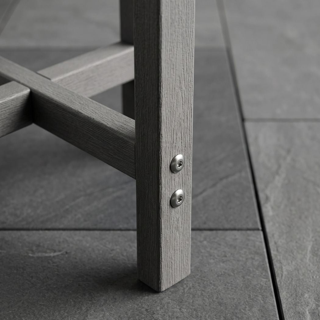 Close-up of a gray wooden outdoor chair leg with two silver screws fastened onto a dark gray tiled floor.