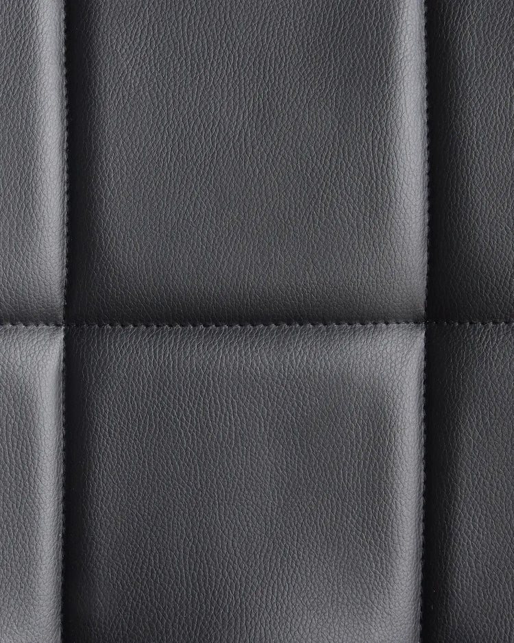 Close-up of a quilted black PVC leather cushion from a modern home office desk chair.