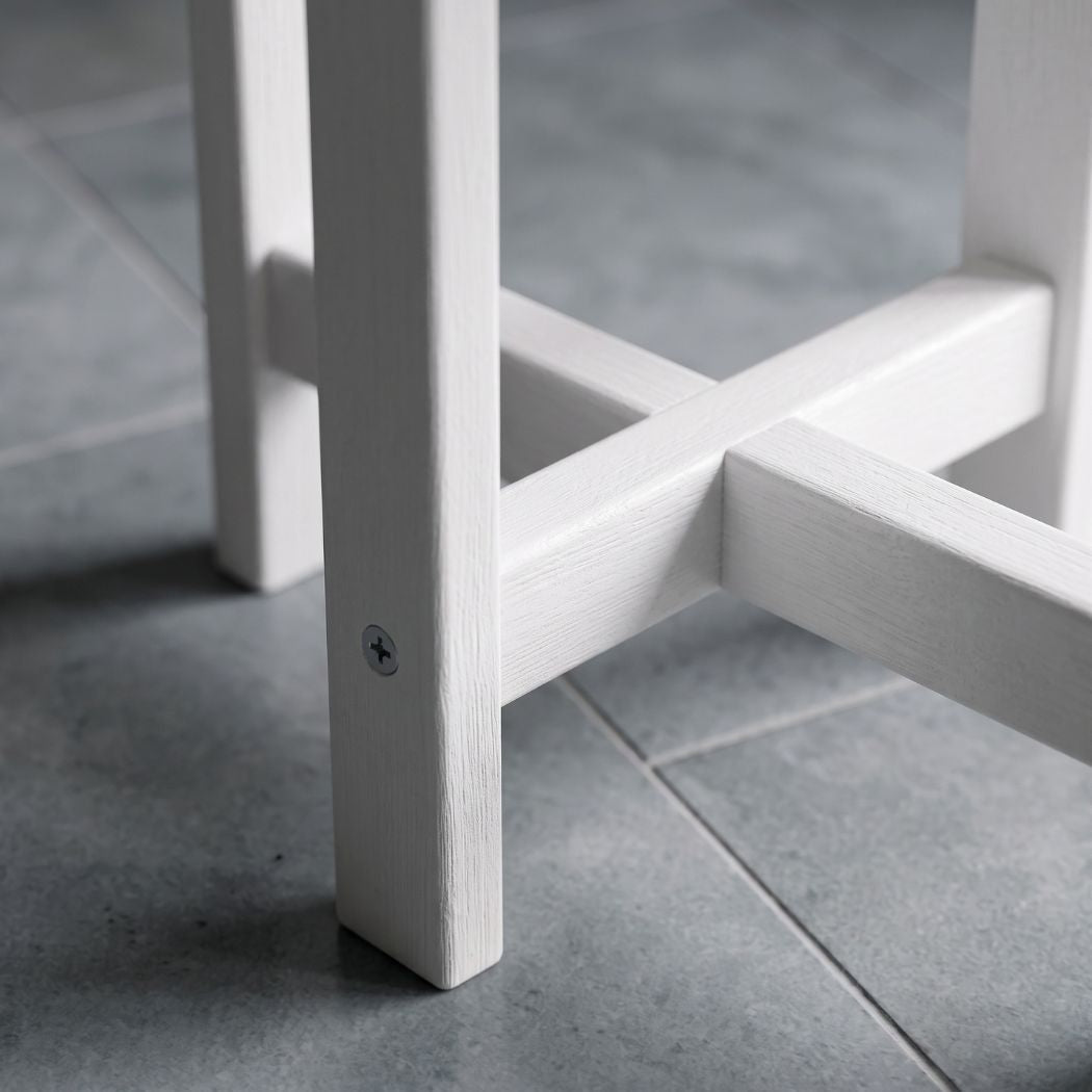 Close-up of a white wooden stool leg and crossbar structure on a gray tiled floor.