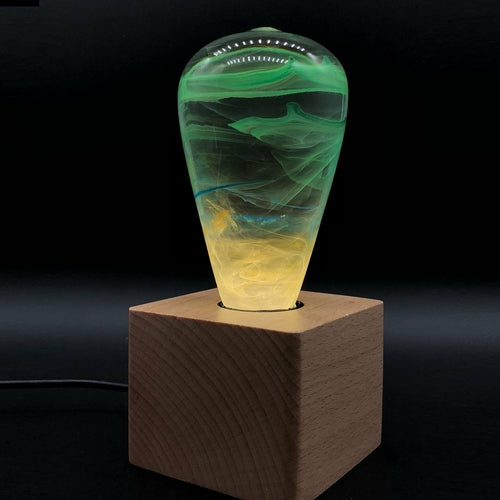 Decorative lamp with green and yellow marbled design on a wooden base against a black background