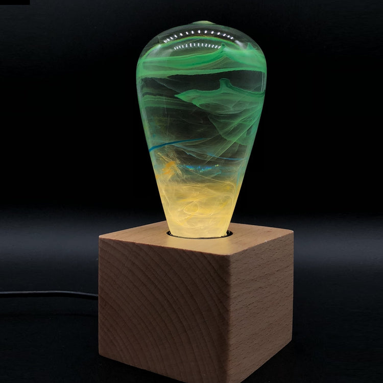 Glass lamp with green and yellow marbled design on a wooden base against a black background