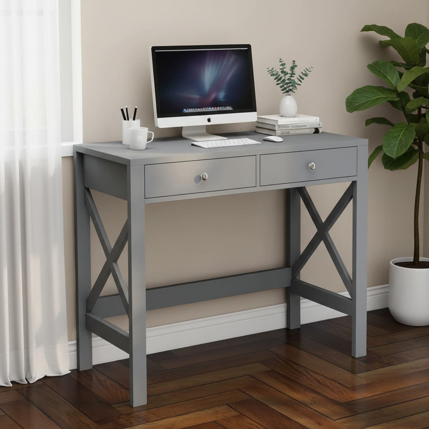 Grey home office desk with two drawers and X-frame, computer monitor, keyboard, plant, and books.