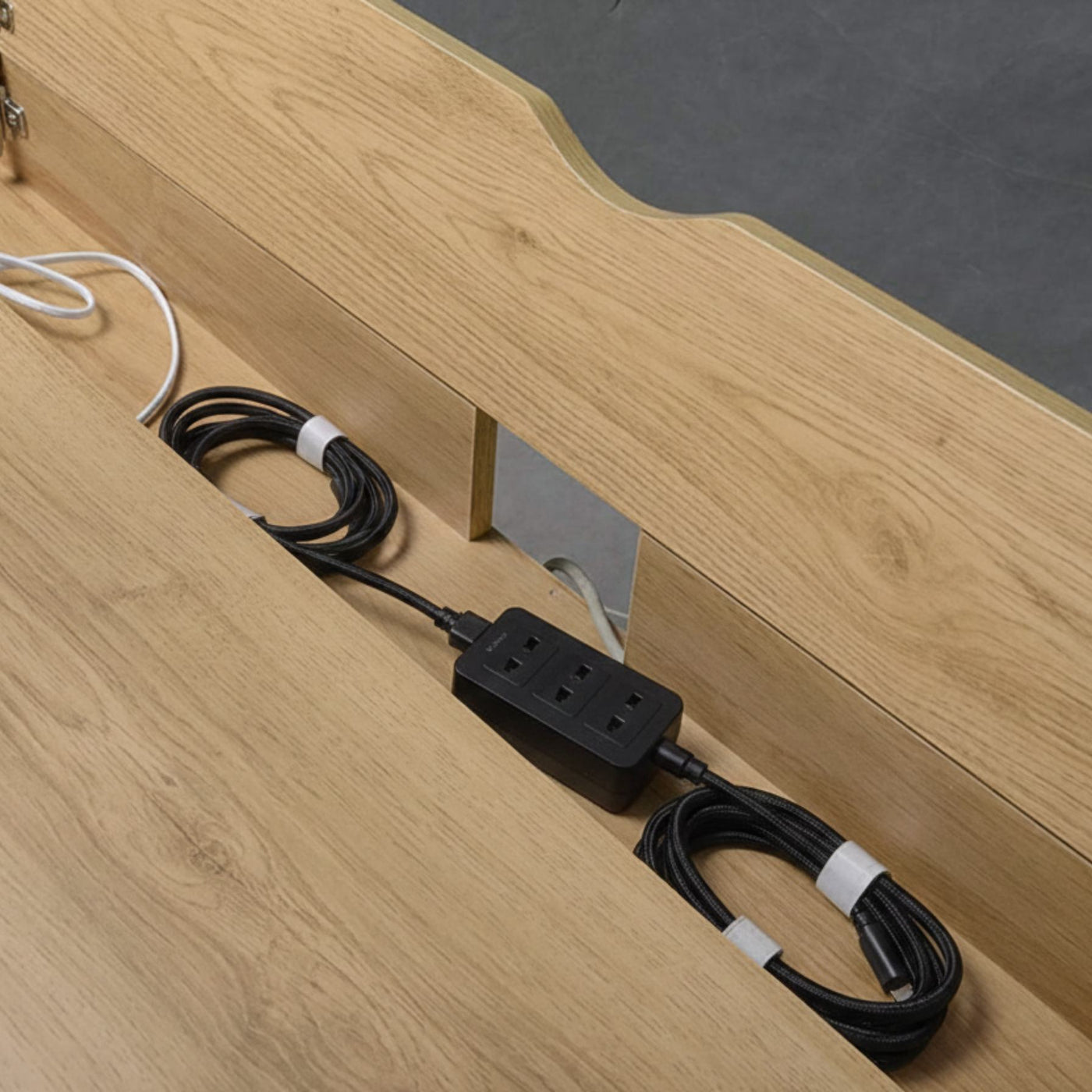 Laptop desk with storage drawer in pine wood finish and visible power strip with coiled cables.