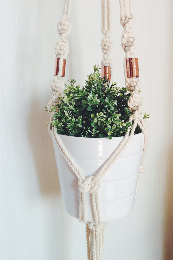 Macrame plant hanger made with locally sourced Ontario cotton rope and copper beads, holding a white pot with greenery.