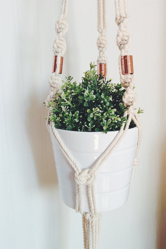Macrame plant hanger made with locally sourced Ontario cotton rope and copper beads, holding a white pot with greenery.