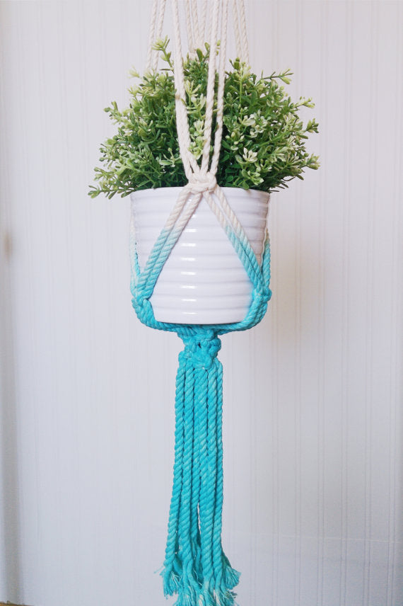 Macrame plant hanger with aquamarine dip-dye cords around a white pot with greenery, handmade in Canada.