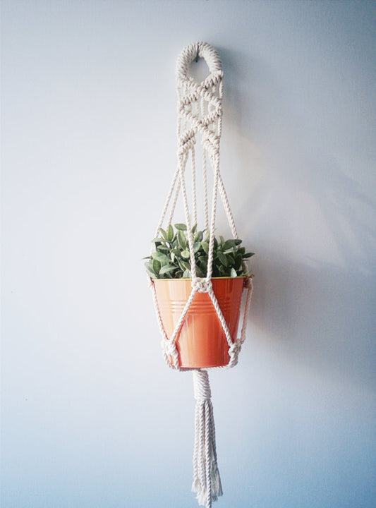 Macrame plant hanger with cotton cord holding an orange pot and green plant.