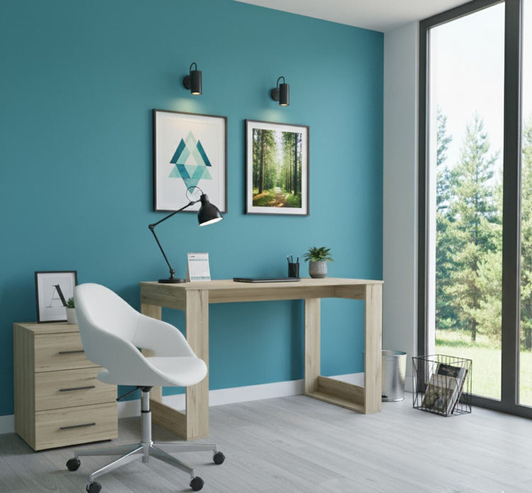 Modern home office with teal walls, wooden desk, white chair, and large windows.
