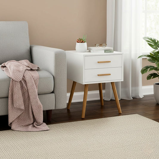 Modern white piano-finish end table with two drawers and angled wooden legs beside a sofa