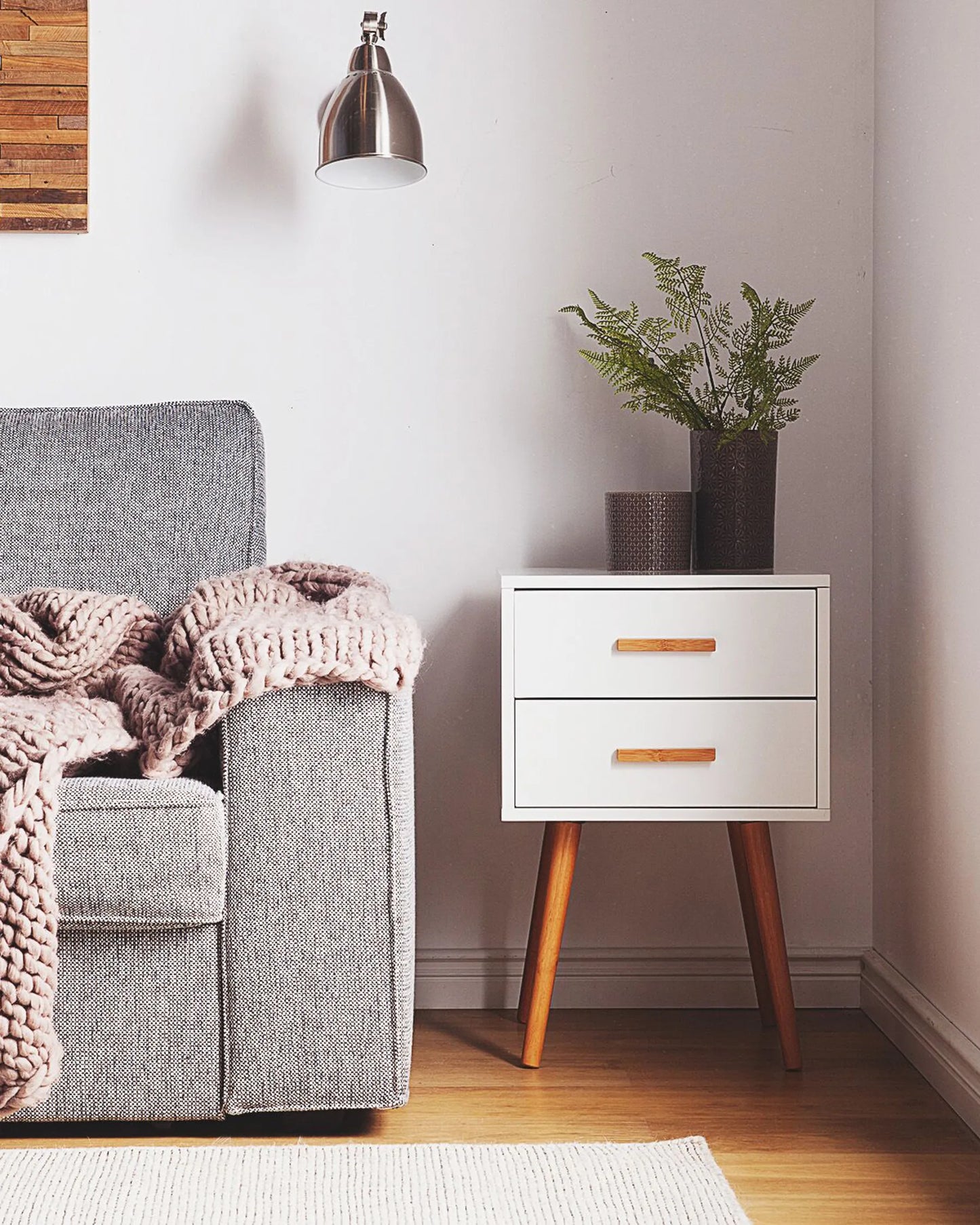 White piano-finish two-drawer end table with tapered wooden legs beside a grey sofa.