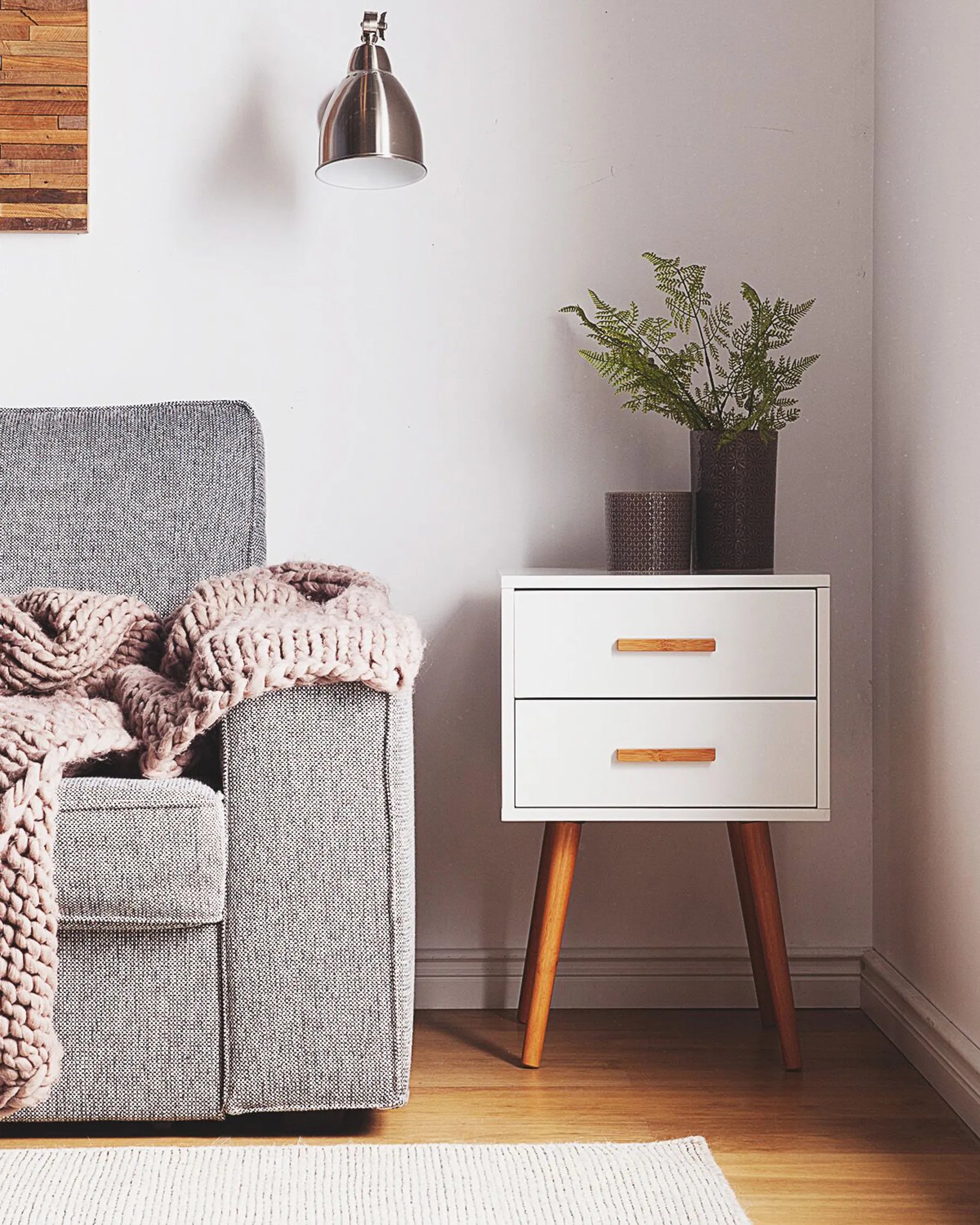 White piano-finish two-drawer end table with tapered wooden legs beside a grey sofa.