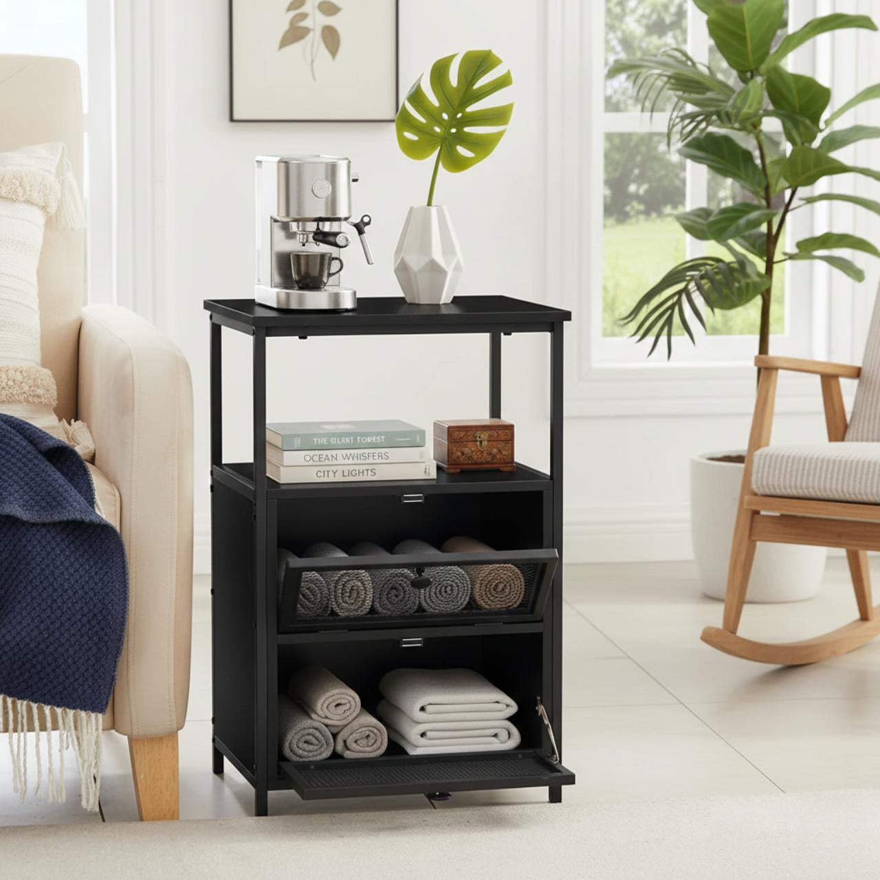 X Design black metal nightstand with flip drawers, coffee maker and vase on top, books and towels stored below.