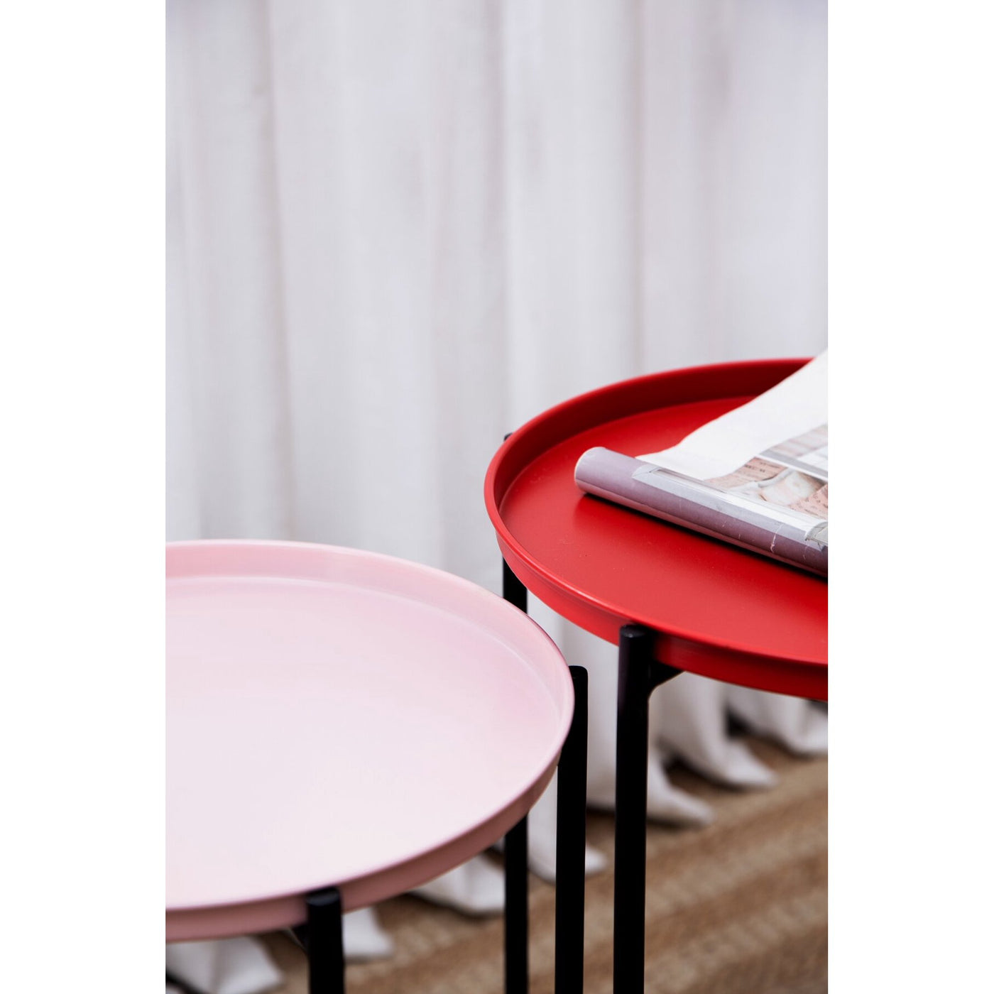 Two round tables, one red and one pink, with a white curtain in the background.