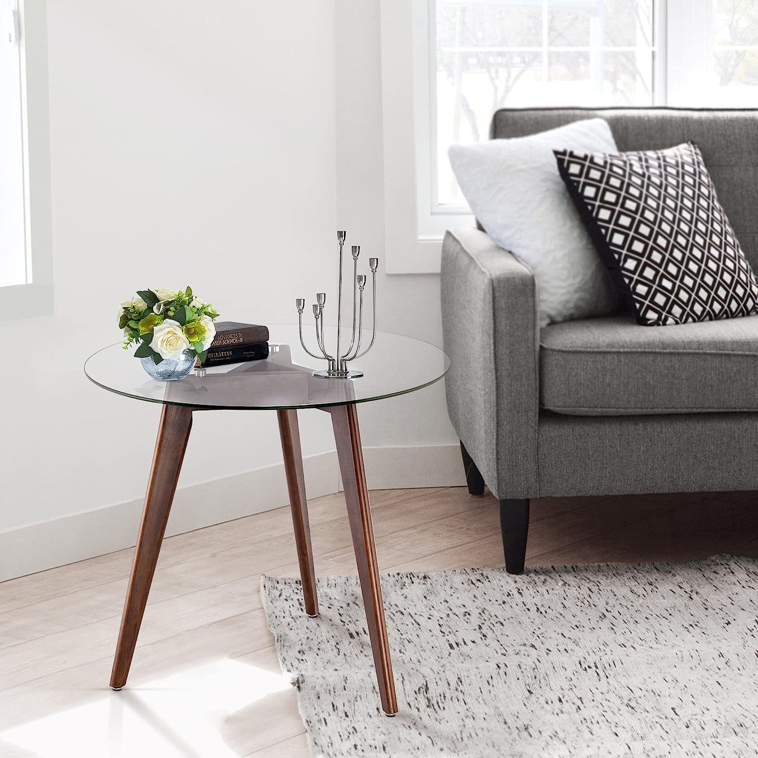 Round tempered glass dining table with 8mm beveled edge and warm oak tripod base in a bright living room.