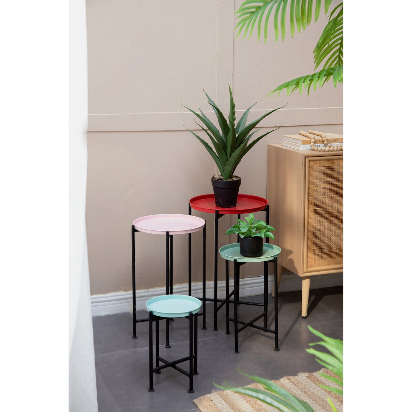 Set of four small round tables with colorful tops in a room with plants and a cabinet.