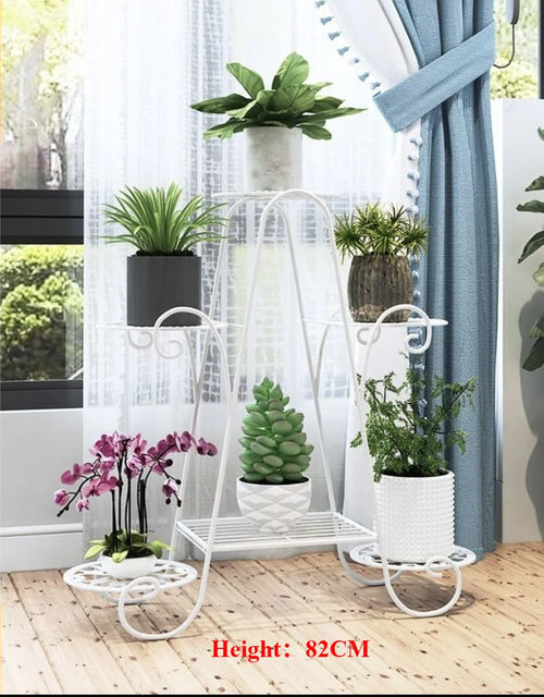Six-tier white metal plant rack with potted plants by a window.