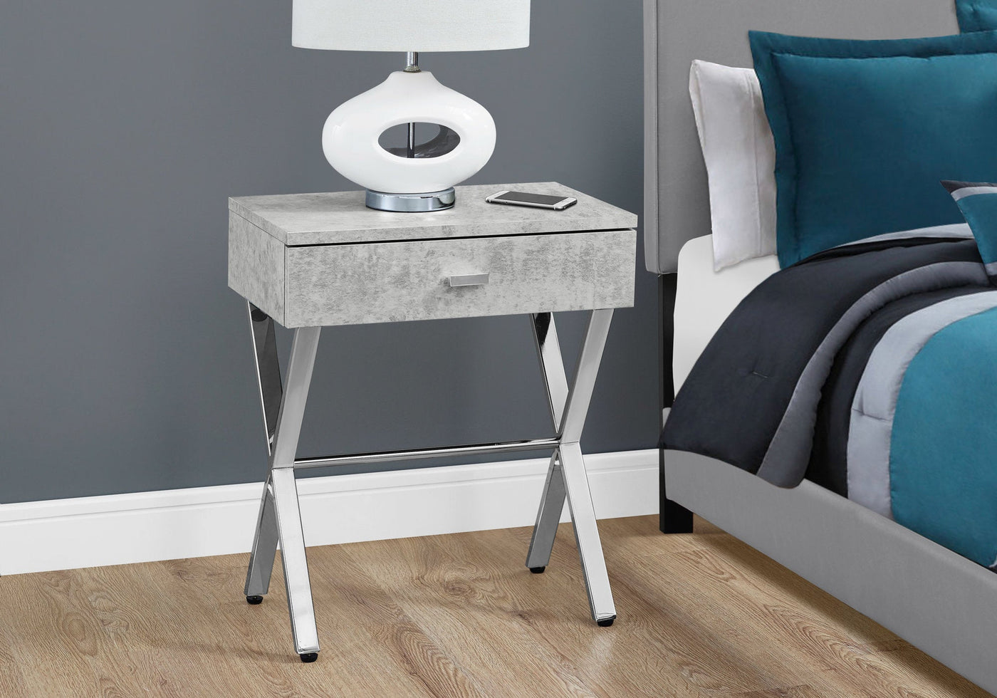 Sleek dark taupe finish accent table with chrome metal legs and a drawer beside a bed.