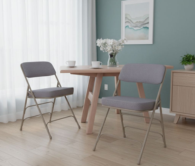Two gray cushioned chairs in front of a wooden table with a vase of flowers on a light wood floor.