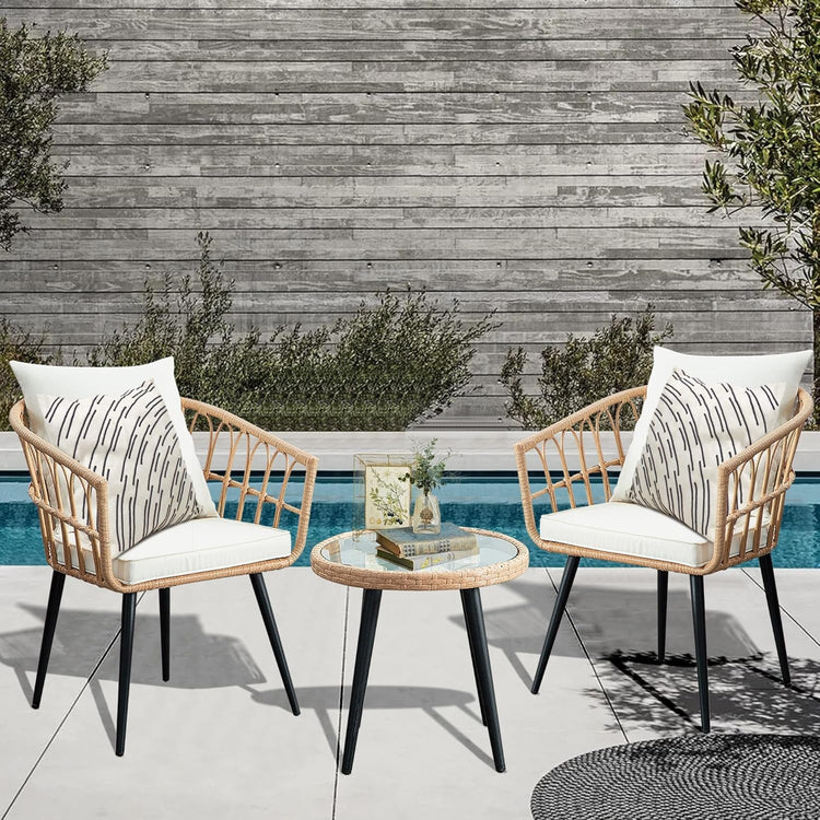 Two wicker chairs with white cushions and a small round table by a poolside.