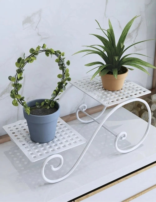 White metal plant stand with two perforated shelves and curved legs, holding two potted plants; space-saving display.