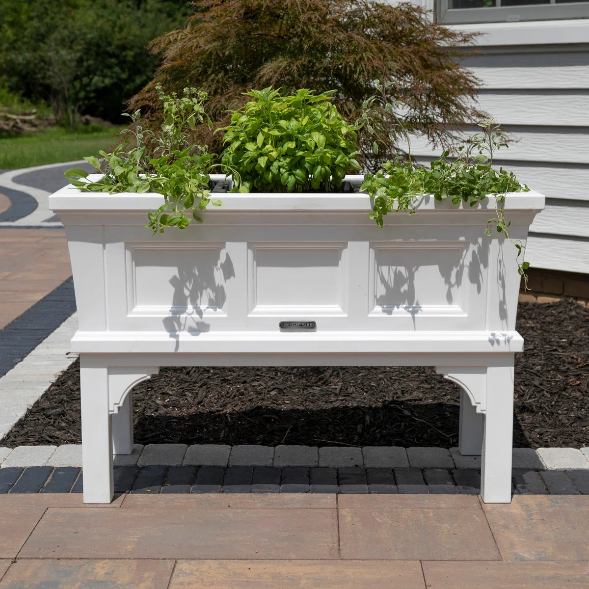 White rectangular raised garden bed planter box on legs with removable trays, filled with herbs.