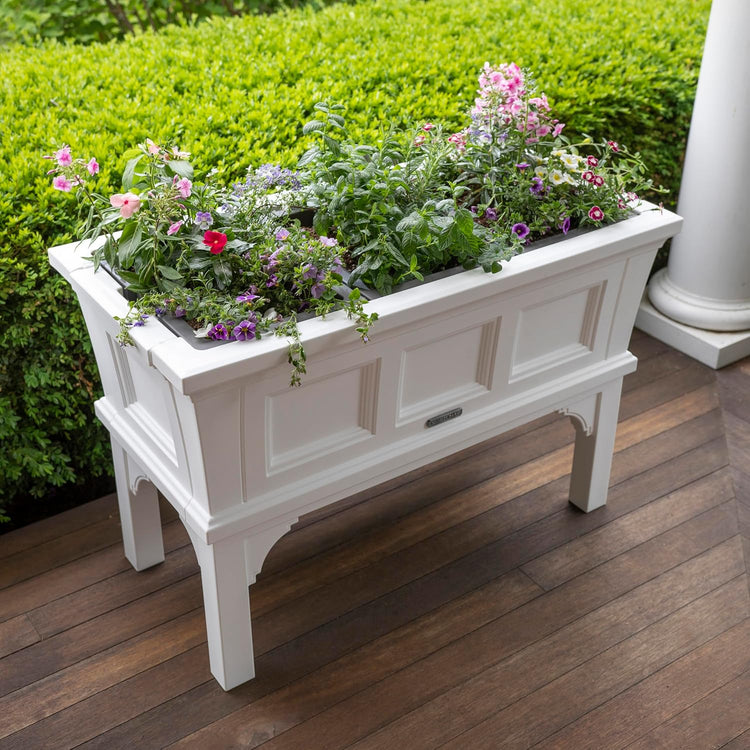 White rectangular raised garden bed planter on legs with removable trays, filled with herbs and flowers.