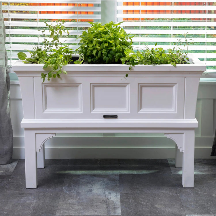 White rectangular raised garden bed planter box on a stand, filled with fresh herbs.