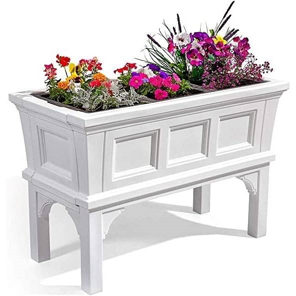 White rectangular raised garden bed planter box on legs with removable trays, filled with colorful flowers.