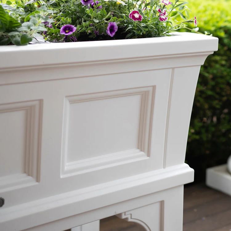 White rectangular raised garden bed planter with removable trays, filled with purple flowers and green foliage.