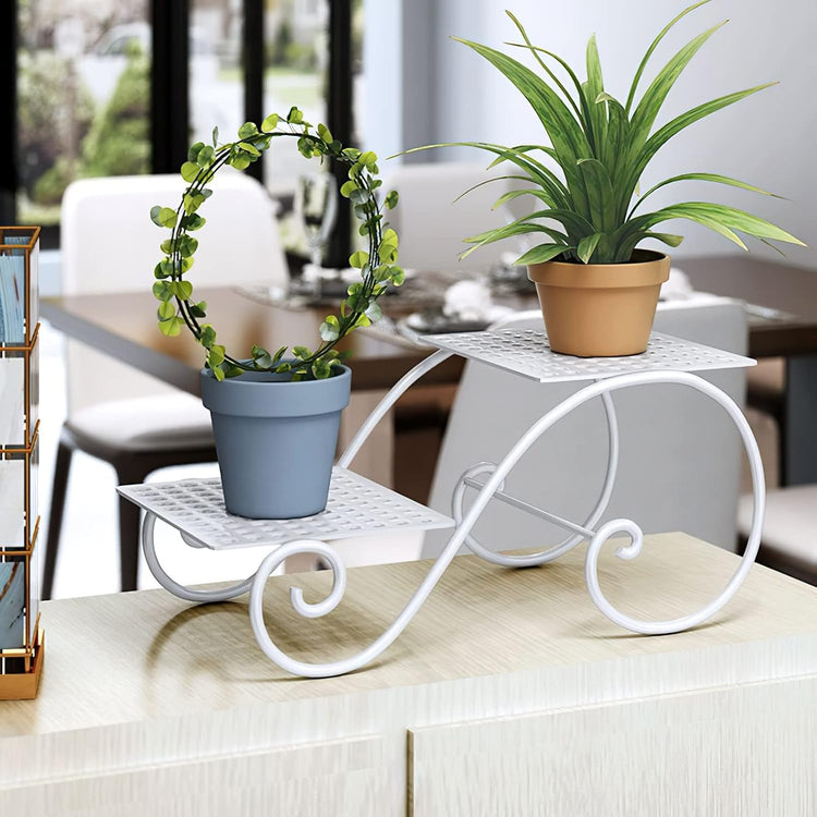 White wrought-iron two-tier plant stand with curved scroll legs, displaying two potted plants on a kitchen counter.