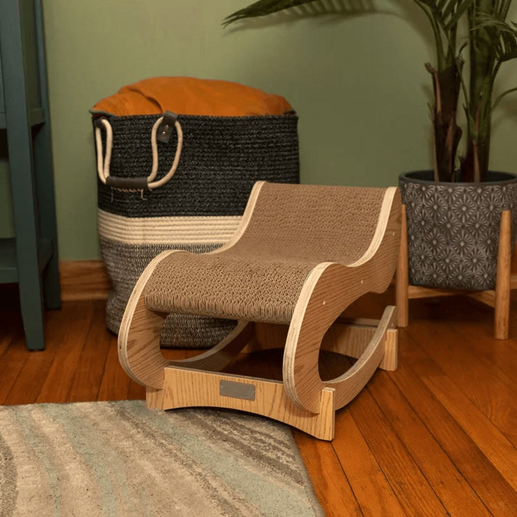 Wooden cat scratcher on a wooden floor with a laundry basket and plant in the background.