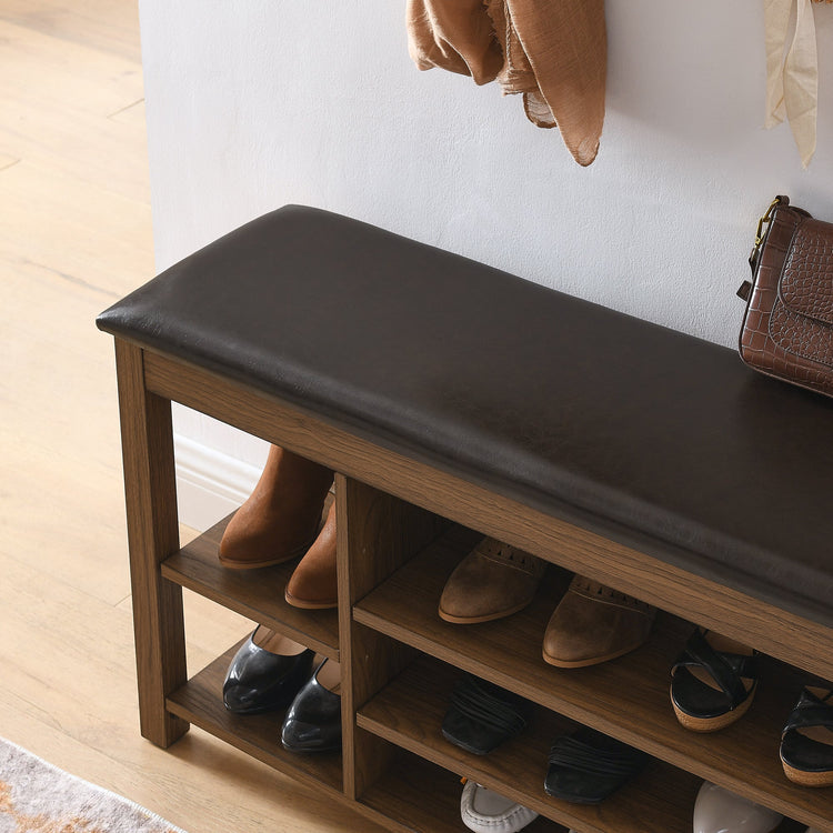 Wooden shoe bench with black cushioned top and open shelves holding shoes in a home setting.