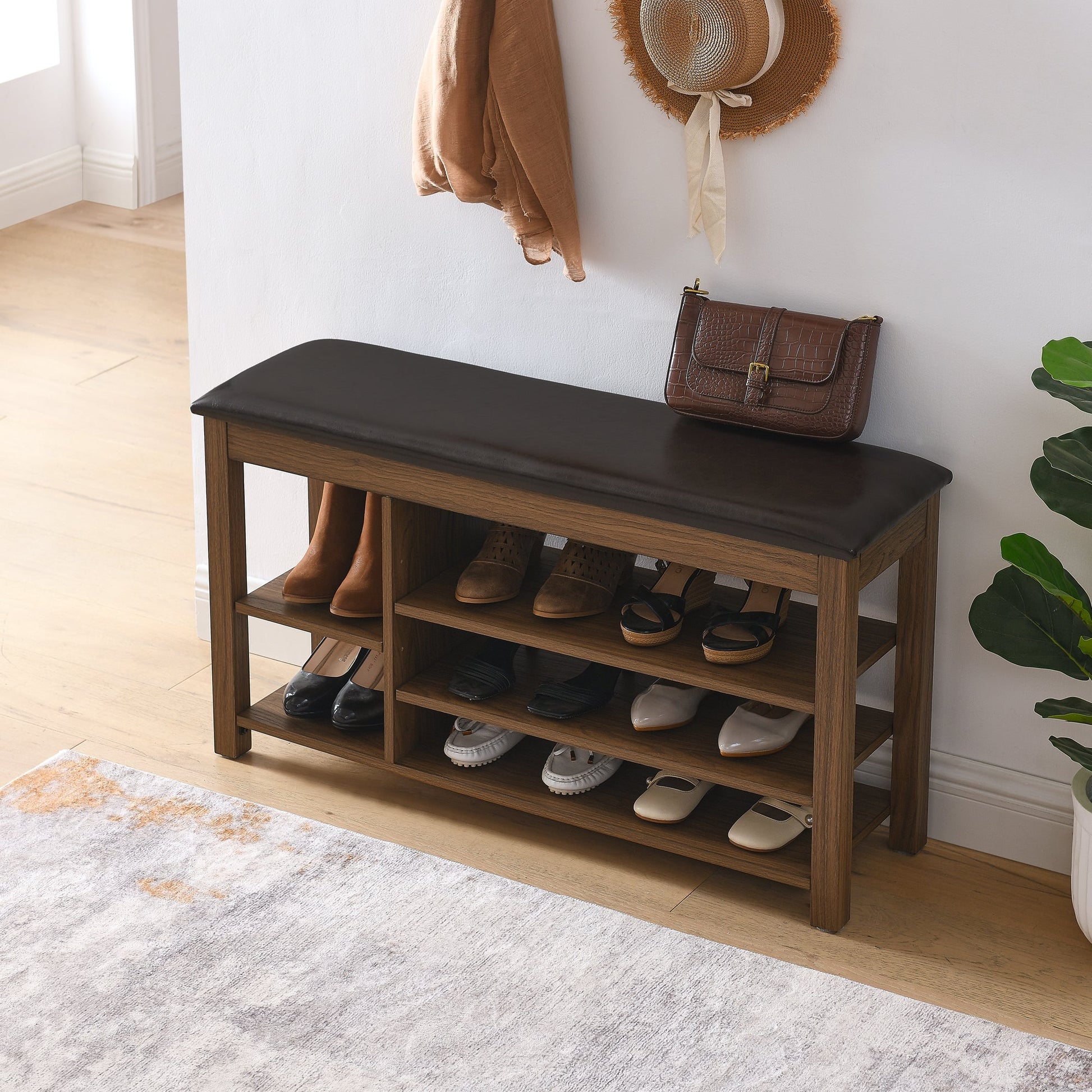 Wooden shoe bench with shoes underneath, coat and hat on wall, plant on side