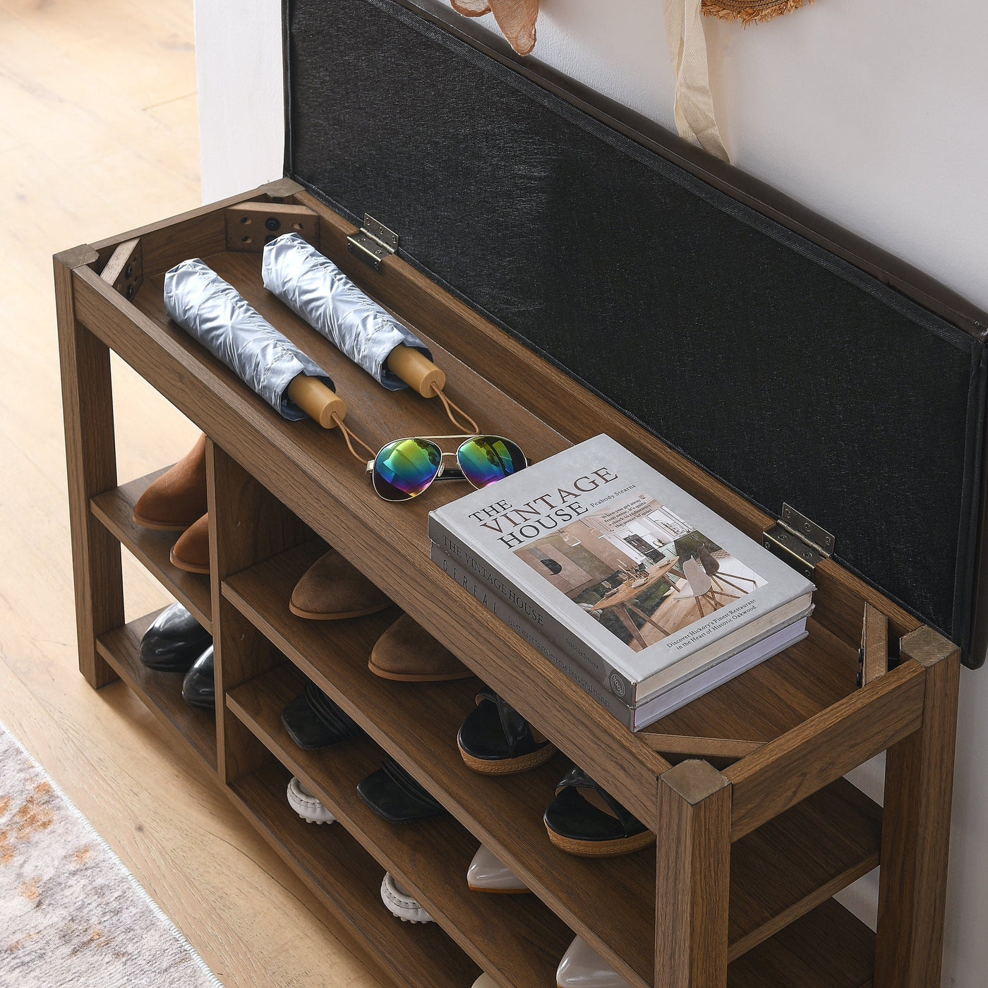Wooden shoe rack with shoes, an umbrella, and a book on a light wooden floor.